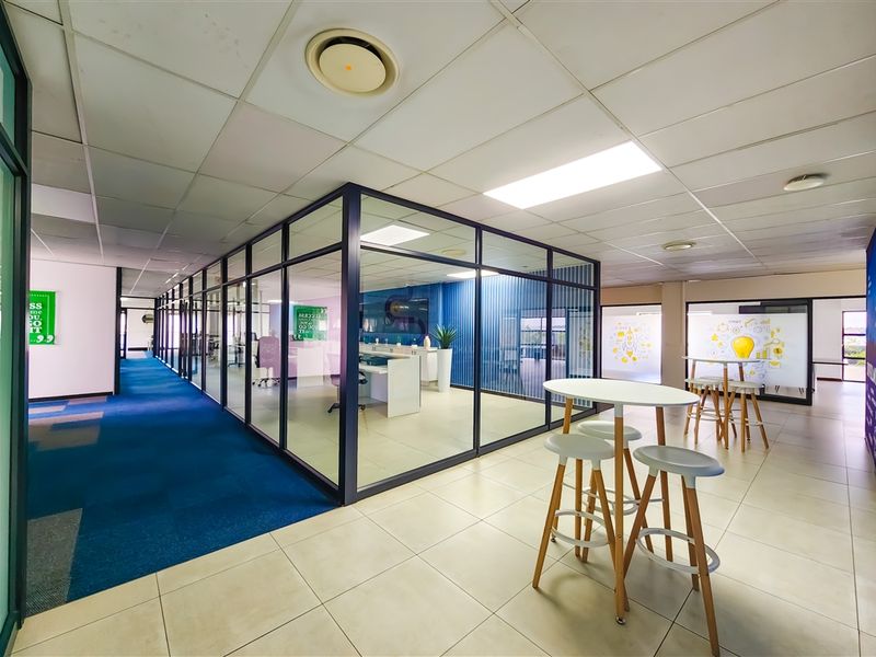 Modern office space featuring glass-partitioned meeting rooms, suspended ceilings with recessed lighting, and a combination of tiled and carpeted flooring.