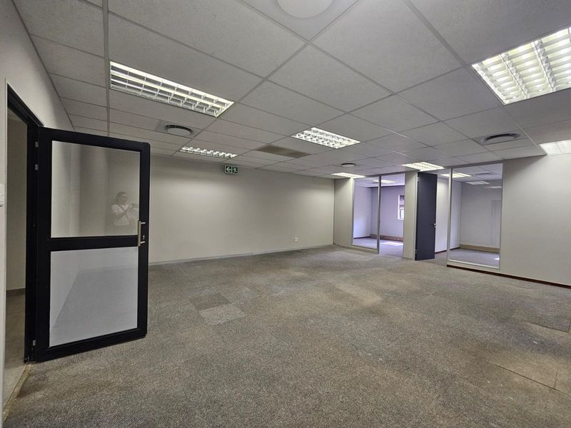 An open-plan office space featuring a suspended ceiling, recessed lighting, and glass partitions, providing a versatile and professional work environment.