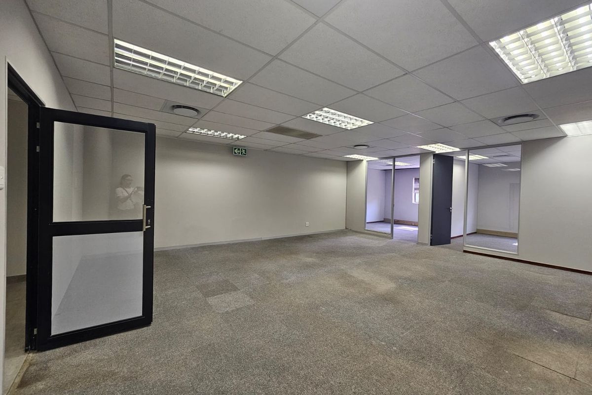 An open-plan office space featuring a suspended ceiling, recessed lighting, and glass partitions, providing a versatile and professional work environment.