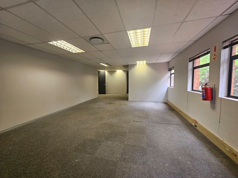 An empty, open-plan office space featuring a suspended ceiling, recessed lighting, and carpeted flooring, suitable for a professional workspace.