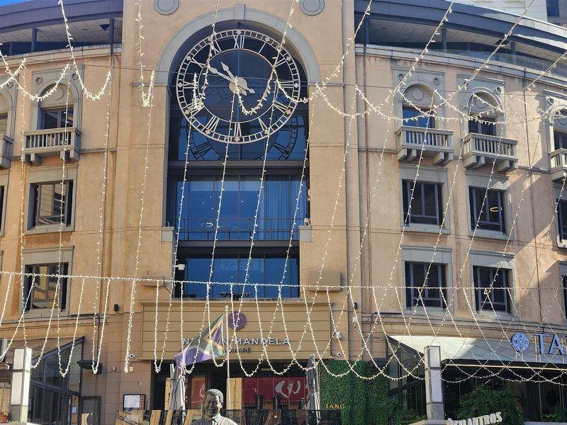 Front elevation of a commercial office building featuring a prominent decorative clock, glass windows, and architectural balconies overlooking the square.