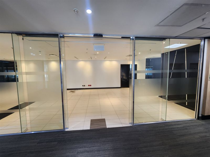 A bright, empty office space featuring modern glass sliding doors, tiled flooring, and recessed ceiling lighting, ready for professional fit-out.