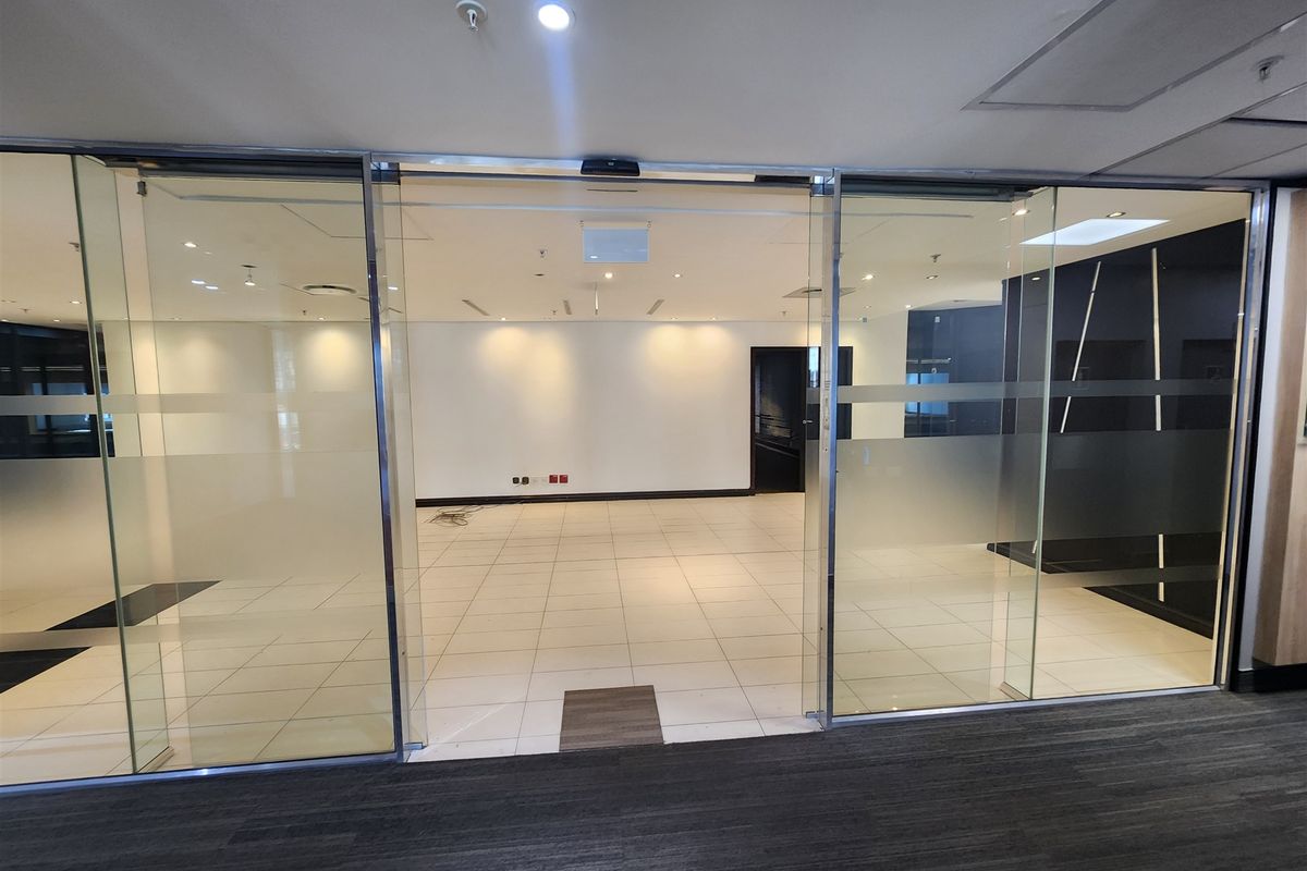 A bright, empty office space featuring modern glass sliding doors, tiled flooring, and recessed ceiling lighting, ready for professional fit-out.