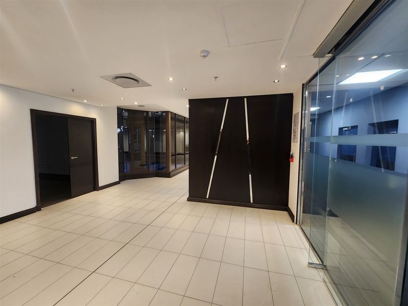 A modern, vacant office lobby or reception area featuring tiled flooring, glass partitions, and a contemporary dark feature wall panel.