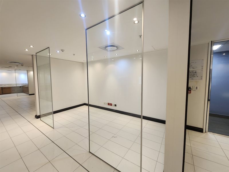 Modern office space featuring glass partition walls, clean white finishes, recessed lighting, and durable ceramic tiled flooring throughout.