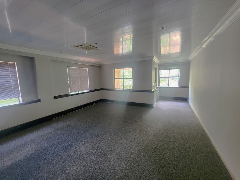 A spacious, empty office area featuring carpeted flooring, recessed ceiling lighting, ducted air conditioning, and multiple windows with venetian blinds.