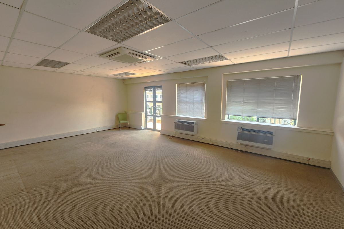 Spacious open-plan office area featuring a suspended ceiling, wall-mounted air conditioning units, and large windows with blinds.
