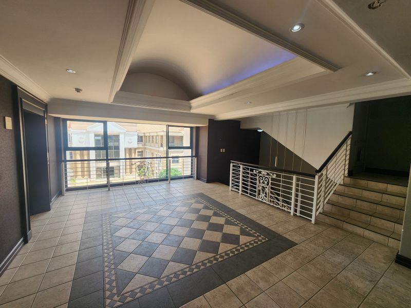 Spacious office entrance foyer featuring a vaulted ceiling, recessed lighting, decorative tiled flooring, and a wrought iron staircase railing.