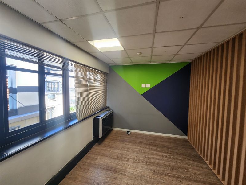 A modern, empty office space featuring wood-look flooring, timber slat wall accents, a suspended ceiling, and a wall-mounted air conditioning unit.