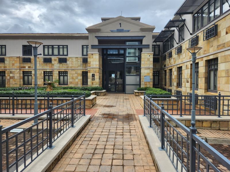 The front entrance of the office building features stone cladding, a paved walkway, and metal railings leading to a glass-paneled main door.