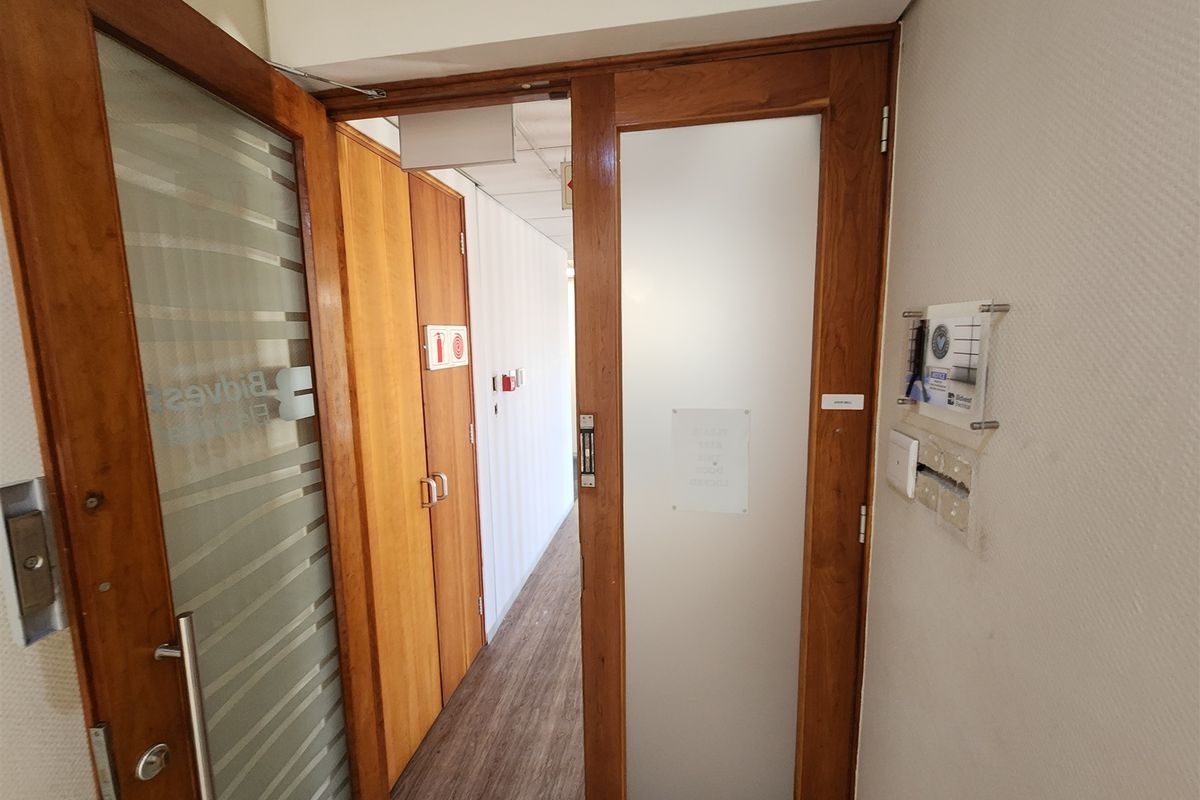 A clean office hallway featuring wood-finish doors, frosted glass panels, and durable laminate flooring, providing a professional and functional transition space.