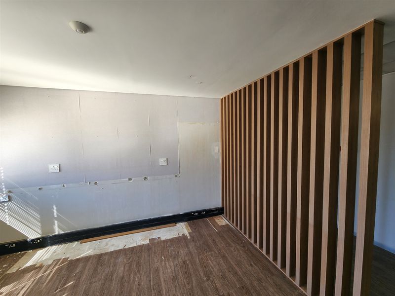 An unfinished office space featuring a modern timber slat room divider, laminate flooring, and exposed wall surfaces requiring final finishing and trim installation.