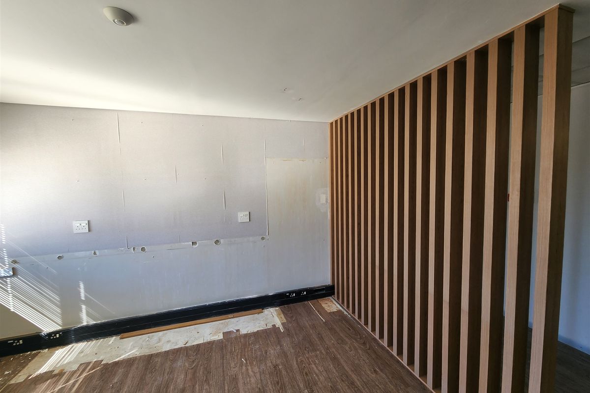 An unfinished office space featuring a modern timber slat room divider, laminate flooring, and exposed wall surfaces requiring final finishing and trim installation.
