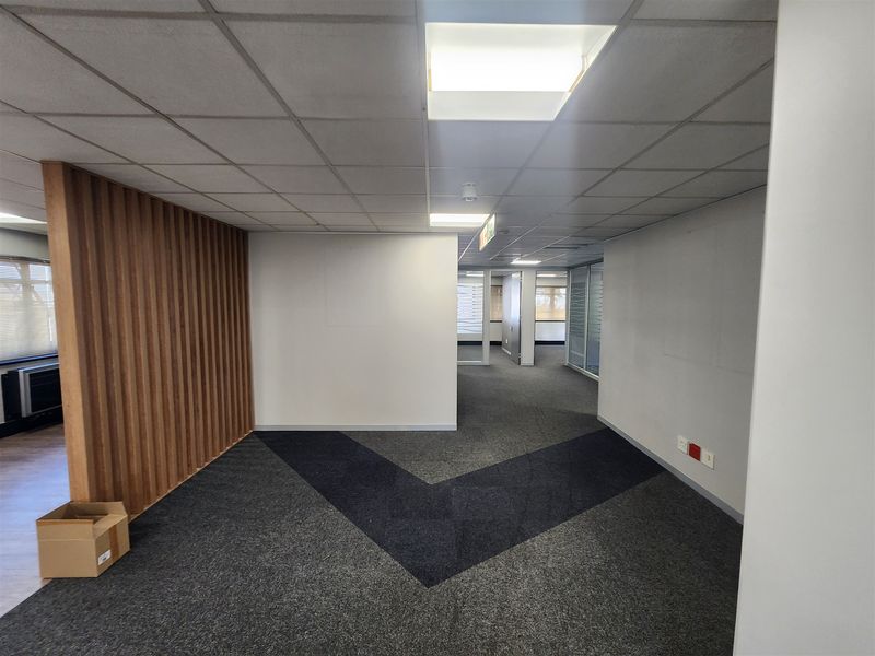 Open-plan office space featuring a modern timber slat feature wall, suspended ceiling with recessed lighting, and durable carpet tile flooring.