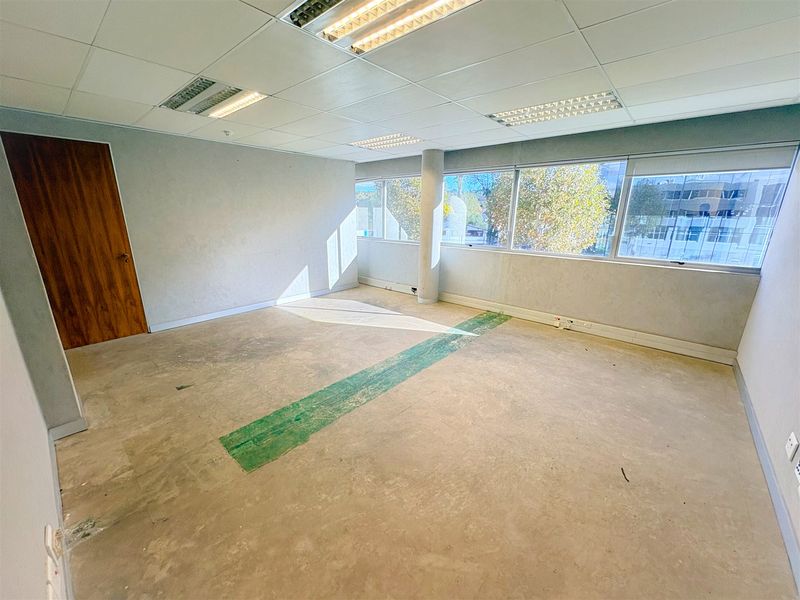 An empty, open-plan office space featuring a suspended ceiling, recessed lighting, and large windows providing natural light. The floor requires finishing.