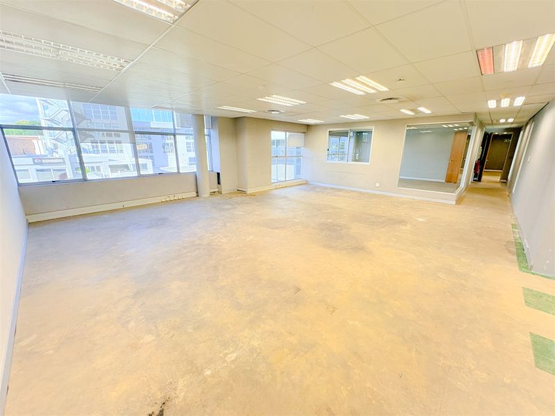 A spacious, vacant open-plan office area featuring large windows, suspended ceilings with recessed lighting, and exposed concrete flooring ready for refurbishment.
