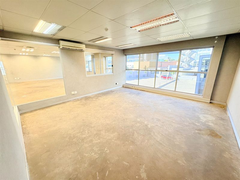 Spacious, empty office suite featuring large windows, suspended ceilings with recessed lighting, a wall-mounted air conditioning unit, and a large feature mirror.