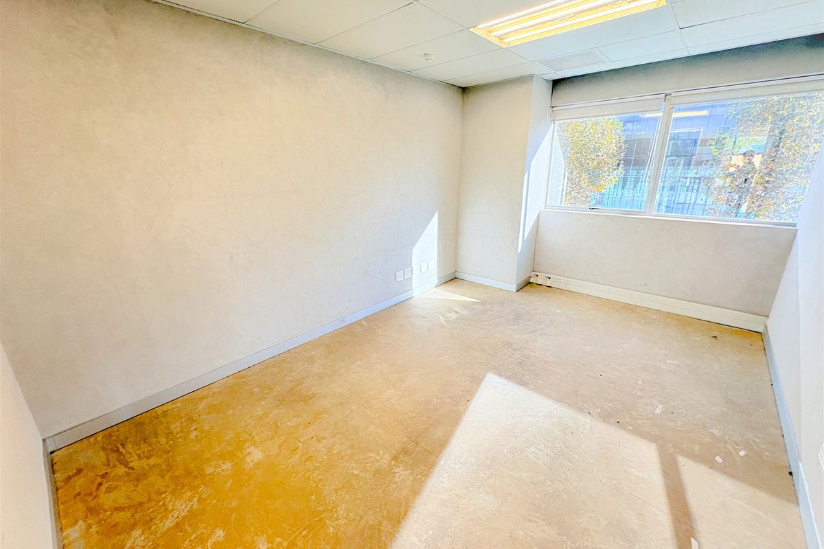 An empty office space featuring a suspended ceiling, fluorescent lighting, and a large window, currently requiring new flooring and wall finishes.