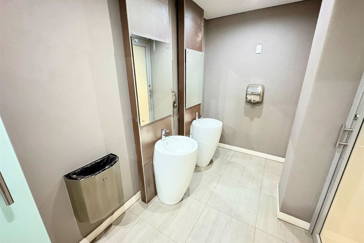 Modern office bathroom featuring dual pedestal washbasins, wall-mounted mirrors, and tiled flooring with integrated wall-mounted dispensers.