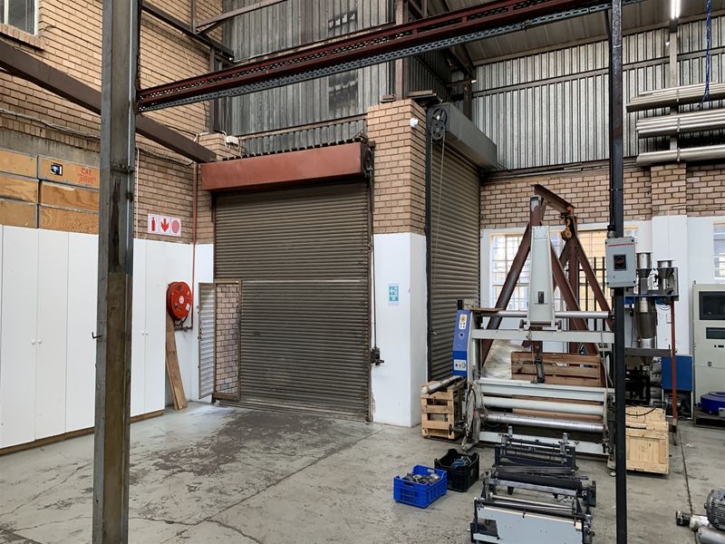 Industrial warehouse space featuring high ceilings, exposed steel structural elements, and a large roller shutter door for vehicle or equipment access.