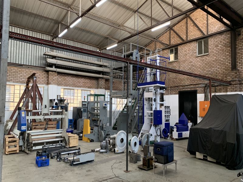 Spacious industrial warehouse facility featuring exposed brick walls, high steel roof trusses, concrete flooring, and an overhead crane rail system.
