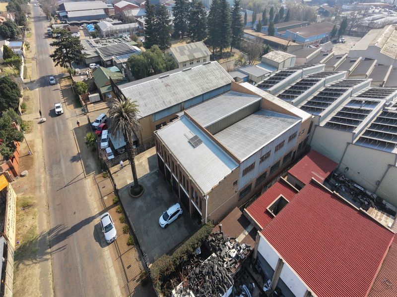 Aerial view of an industrial property featuring multiple warehouse structures with corrugated metal roofing, brick facades, and a concrete driveway.