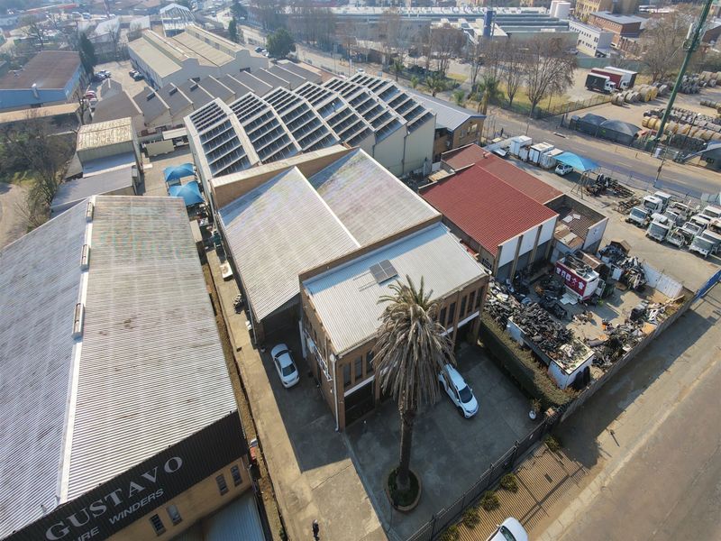 Aerial view of an industrial property featuring multiple warehouse buildings with corrugated metal roofing, solar panel installations, and a paved yard area.