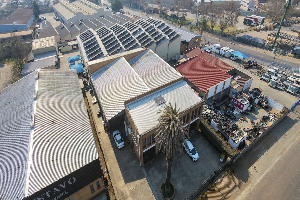 Aerial view of an industrial property featuring multiple warehouse buildings with corrugated metal roofing, solar panel installations, and a paved yard area.