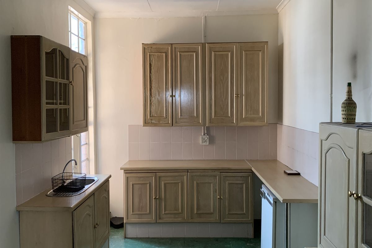 A dated kitchen area featuring traditional built-in cabinetry, laminate countertops, and a tiled backsplash, offering potential for a modern renovation.