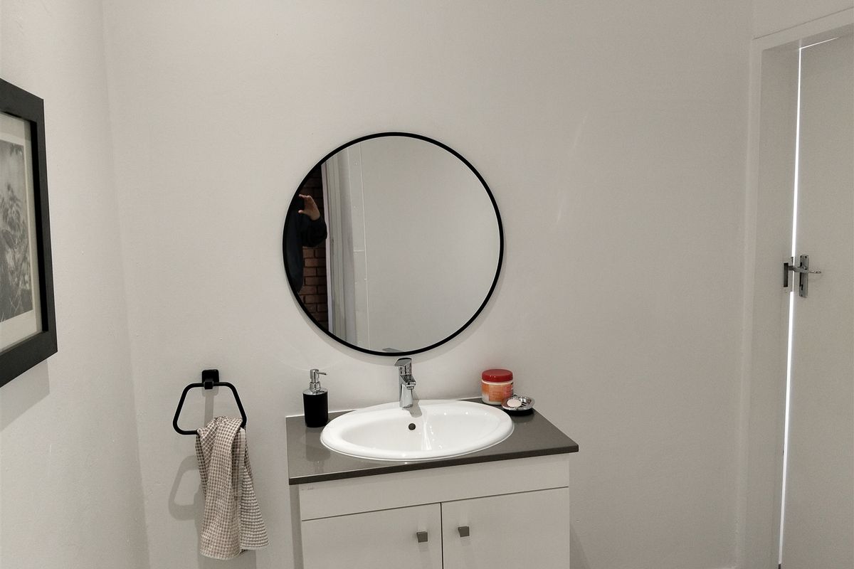 A clean and modern bathroom vanity area featuring a white cabinet, integrated basin, and a circular wall-mounted mirror.