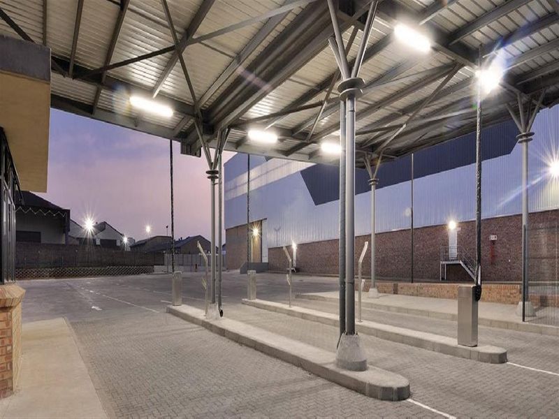 A well-maintained commercial exterior featuring a large covered paved area with steel structural supports and industrial lighting.