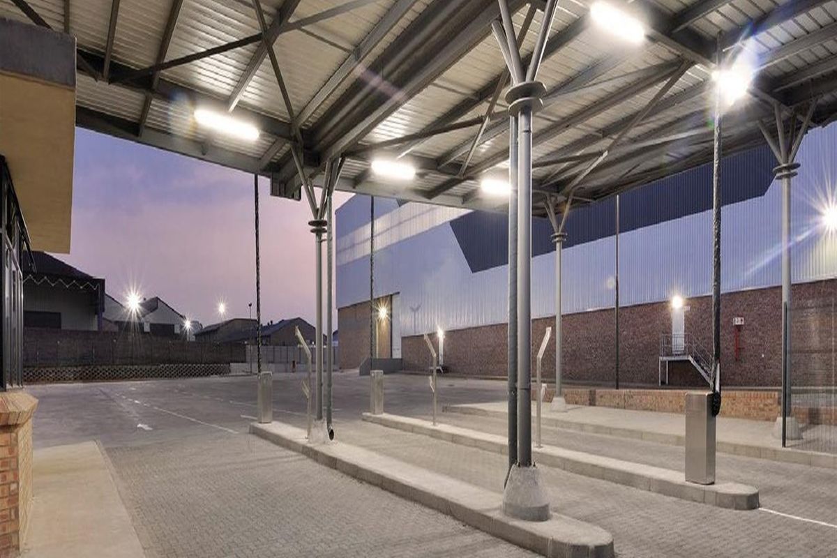 A well-maintained commercial exterior featuring a large covered paved area with steel structural supports and industrial lighting.