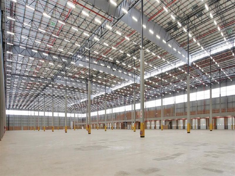 Expansive industrial warehouse space featuring high ceilings, steel truss roofing, integrated sprinkler systems, and multiple loading docks on a polished concrete floor.