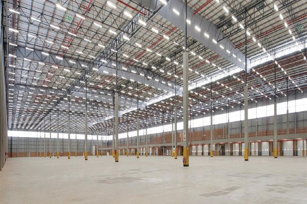 Expansive industrial warehouse space featuring high ceilings, steel truss roofing, integrated sprinkler systems, and multiple loading docks on a polished concrete floor.