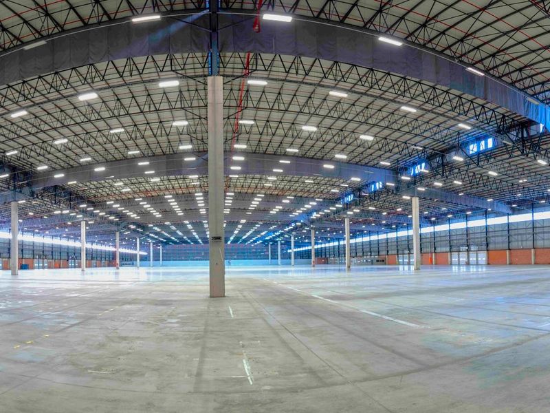 A vast, open-plan industrial warehouse space featuring high ceilings, durable concrete flooring, extensive LED lighting, and a robust steel truss roof structure.