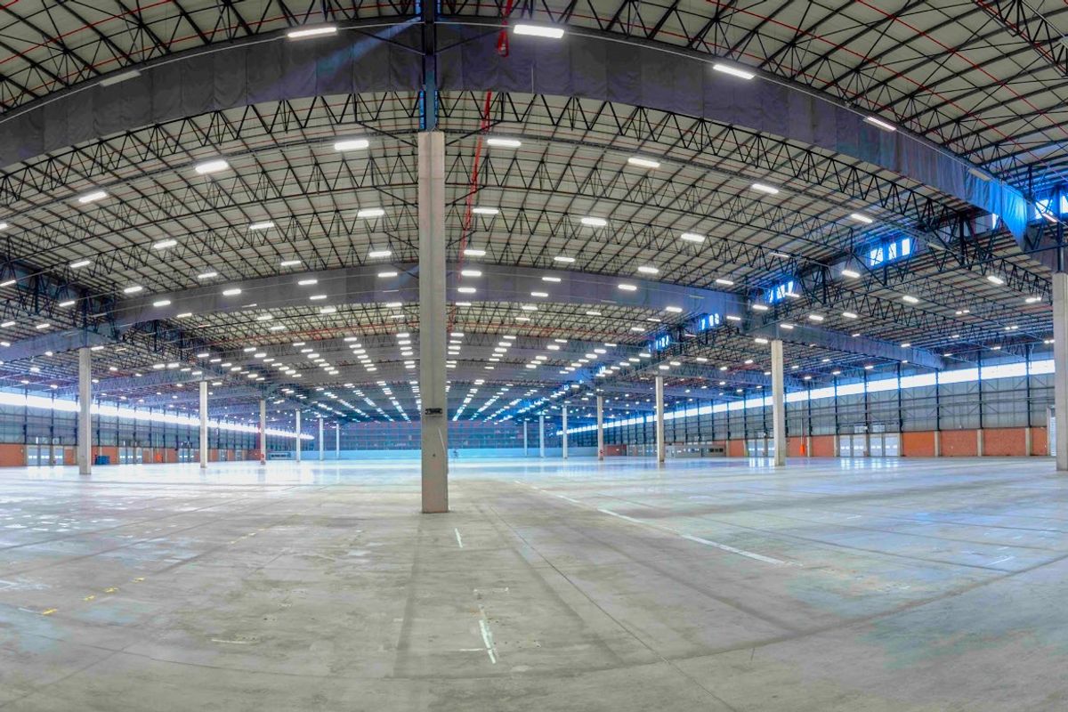 A vast, open-plan industrial warehouse space featuring high ceilings, durable concrete flooring, extensive LED lighting, and a robust steel truss roof structure.