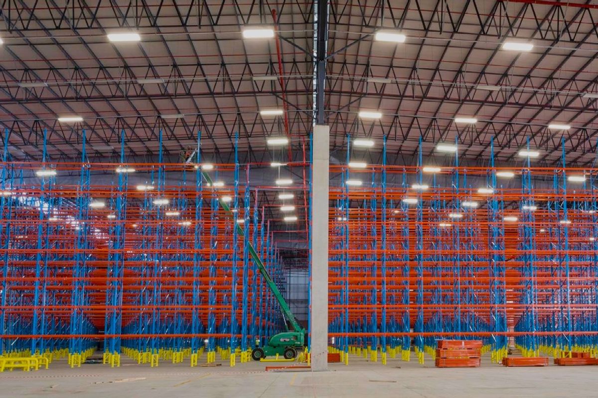 Expansive industrial warehouse space featuring high-clearance ceilings, extensive steel racking systems, polished concrete flooring, and modern overhead lighting.