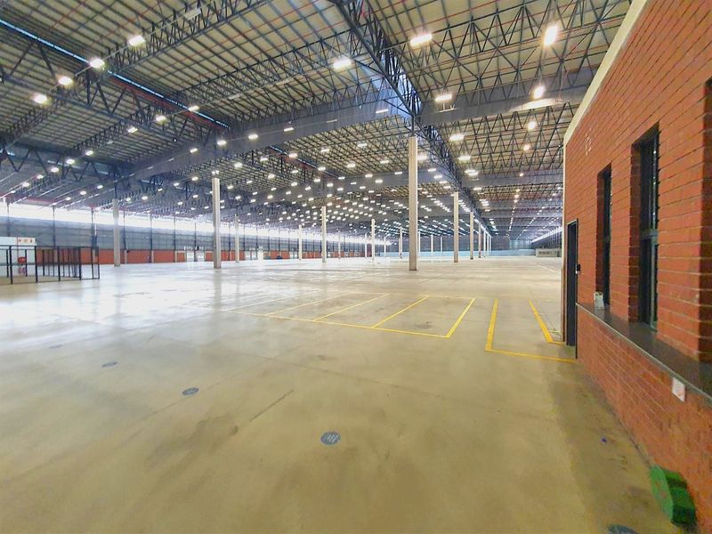 Expansive industrial warehouse space featuring high ceilings with exposed steel trusses, high bay lighting, and durable concrete flooring.