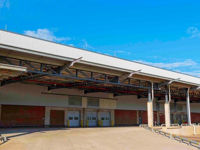 Industrial warehouse exterior featuring multiple loading docks, a large concrete apron, and an extensive steel canopy for sheltered loading operations.