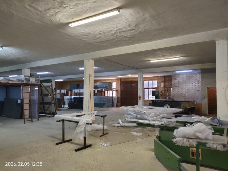 Spacious industrial utility area featuring exposed brickwork, concrete flooring, structural support columns, and functional overhead fluorescent lighting.