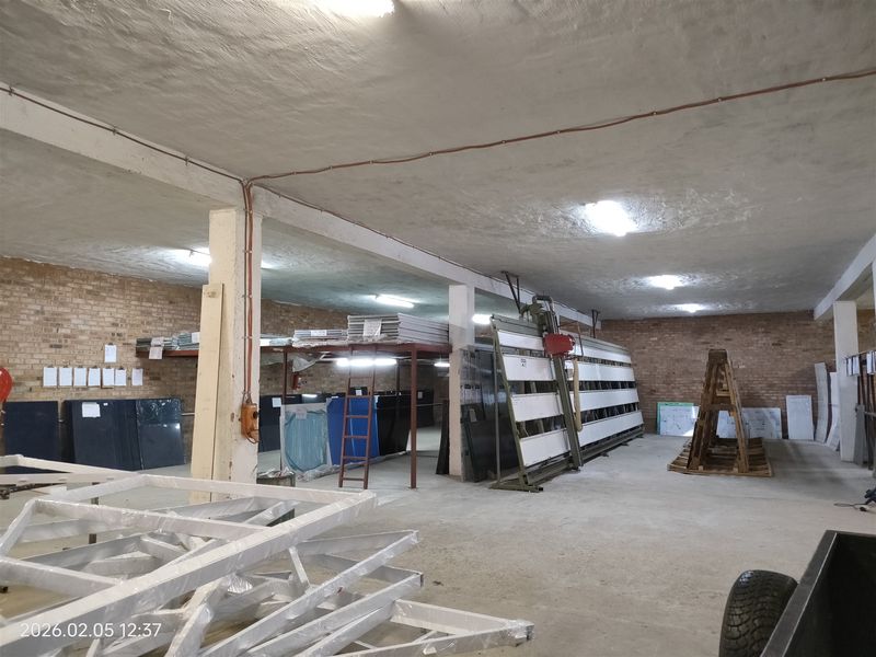 Spacious industrial utility or warehouse area featuring exposed brick walls, concrete flooring, and structural support columns, suitable for storage or manufacturing operations.