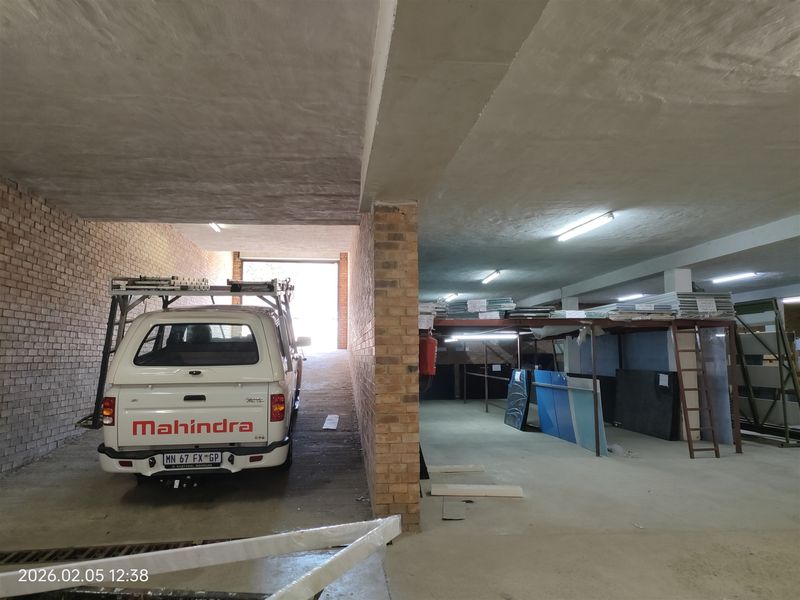 Spacious industrial garage or warehouse area featuring exposed brick walls, concrete flooring, and overhead fluorescent lighting with integrated steel storage racking.