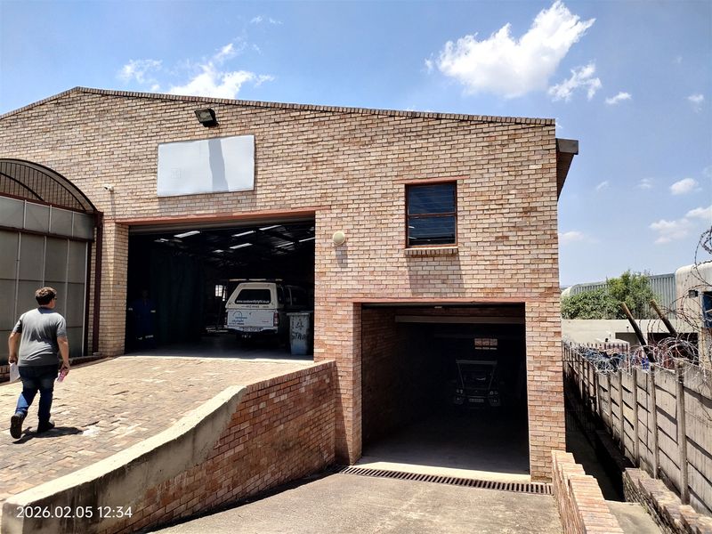 Industrial property featuring a face brick facade, large roller shutter door access, and a dedicated underground parking entrance with security fencing.