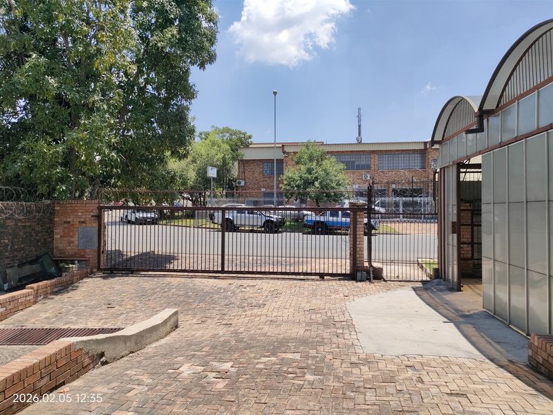 Front exterior view of the industrial property featuring a secure metal gate, brick paved driveway, and perimeter security fencing.