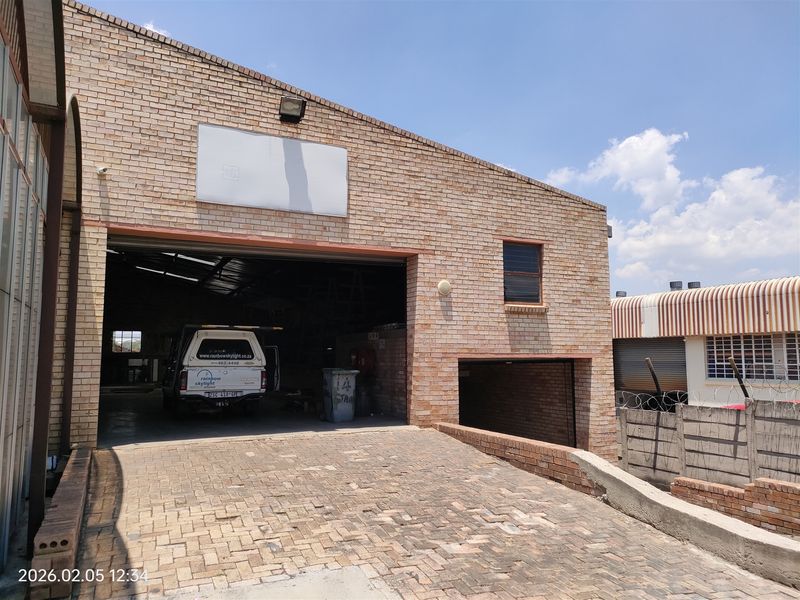Industrial property featuring a face brick facade, large roller shutter door access, and a paved driveway with perimeter security walling.