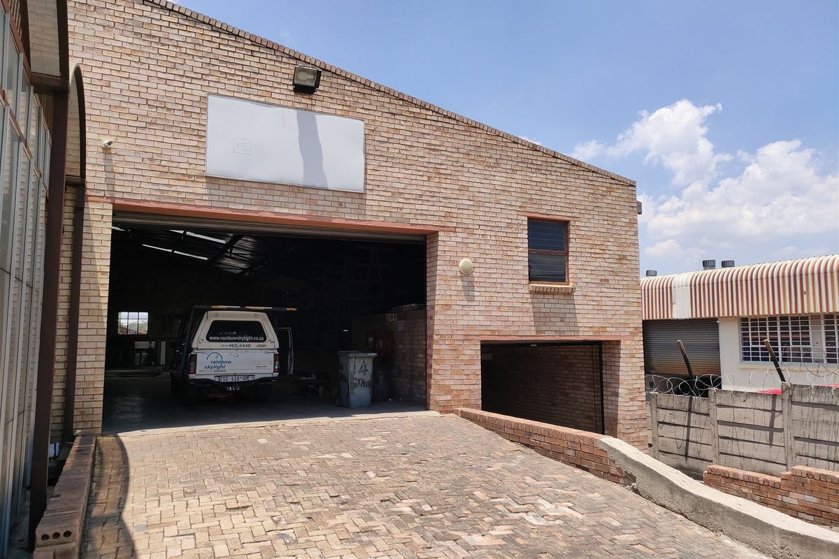 Industrial property featuring a face brick facade, large roller shutter door access, and a paved driveway with perimeter security walling.