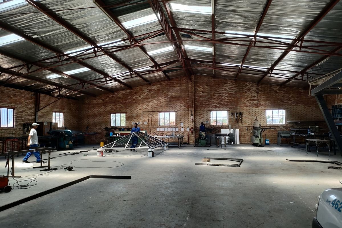 Spacious industrial workshop featuring exposed brick walls, high-clearance steel roof trusses with integrated skylights, and durable concrete flooring suitable for manufacturing or storage.