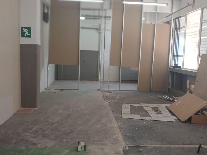 Industrial interior space currently undergoing renovation, featuring exposed metal partition framing, unfinished flooring, and industrial lighting fixtures.