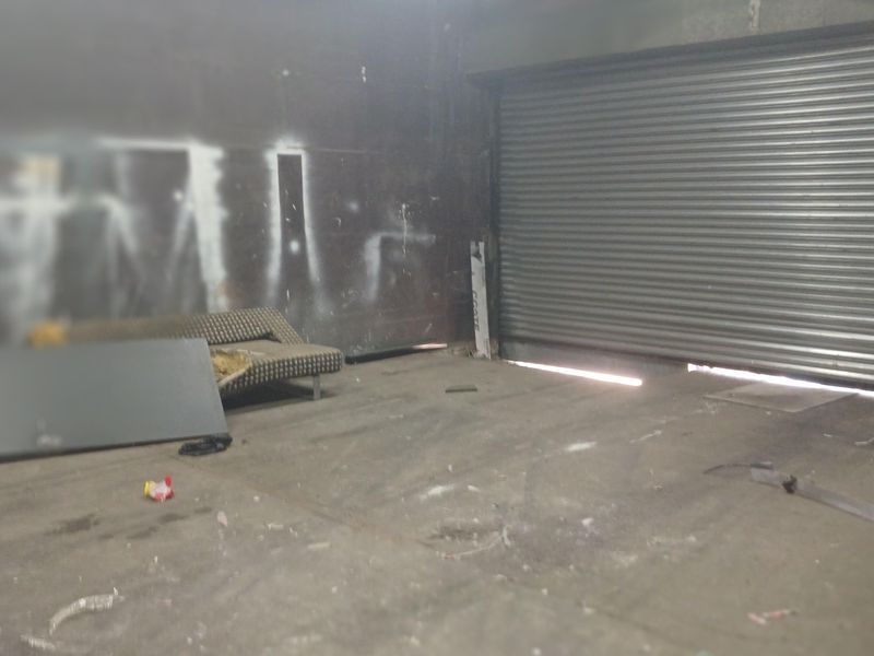 Industrial garage space featuring a large roller shutter door, concrete flooring, and exposed structural elements, currently in need of maintenance and cleaning.