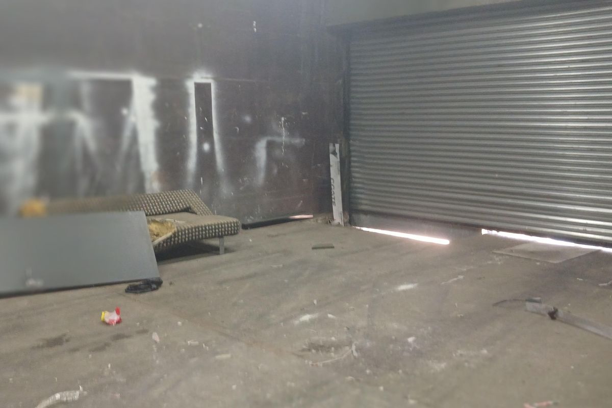 Industrial garage space featuring a large roller shutter door, concrete flooring, and exposed structural elements, currently in need of maintenance and cleaning.